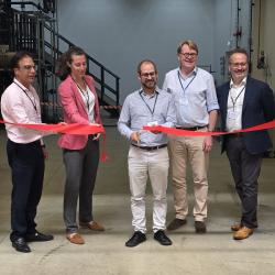 five people cut a red ribbon to open a new facility.