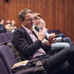 Prof Clemens Kaminski in a lecture theatre seating with a microphone asking a question of someone off camera.