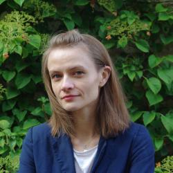 Ewa Marek in blue blazer and white tshirt headshot in front of green leaf background.