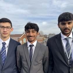 Three young men in suits, school students, stood with a red brick building in the background
