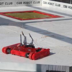 A small red robot stands in a custom-built arena. Text around the border of the arena reads 'CEB Robot Club'