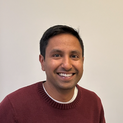 Man in red jumper smiling at camera in white room.