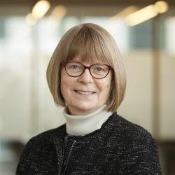 Lynn Gladden in glasses and professional office attire smiles at the camera in a headshot with a blurred background.