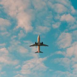 A plane flies across a lightly clouded sky