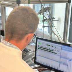 Man's back to camera as he looks at computer with scientific results on, woman side on in edge of photo
